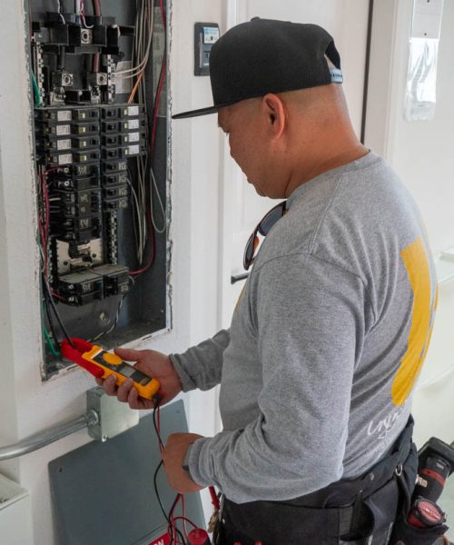 An electrician checks electrical connections within a panel using a multimeter, highlighting thorough electrical safety inspections.