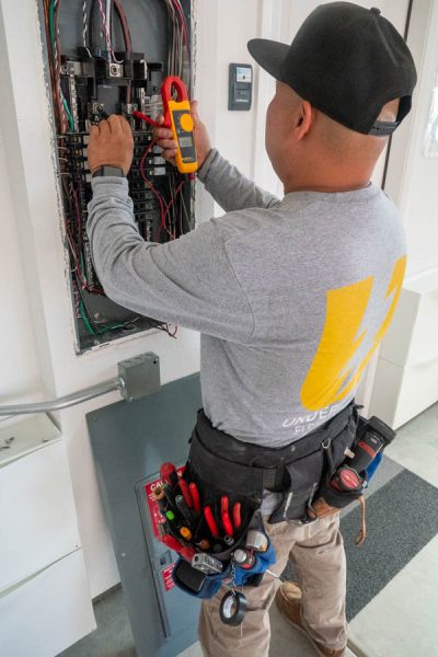 An electrician uses a multimeter to test circuits within an electrical panel, showcasing expertise in electrical maintenance and safety evaluations.