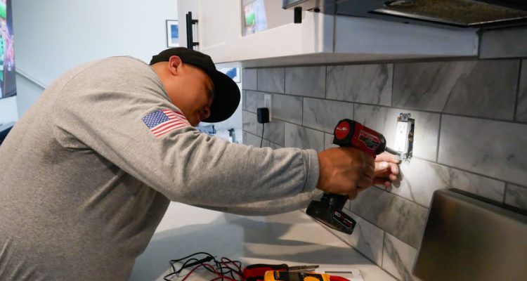 An electrician works on installing a new outlet in a kitchen, highlighting his detailed approach to residential electrical services.
