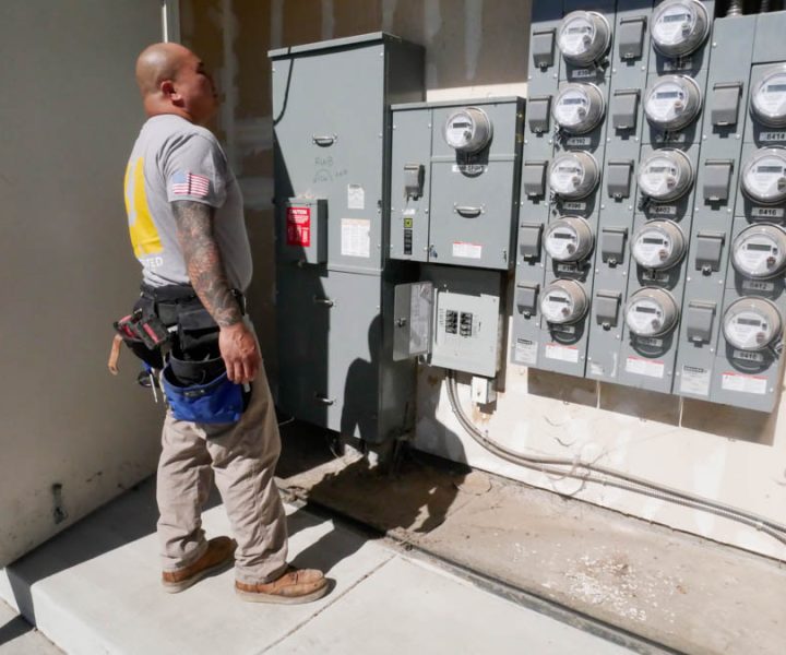 An electrician inspects a bank of commercial electric meters, demonstrating expertise in commercial electrical services and maintenance.